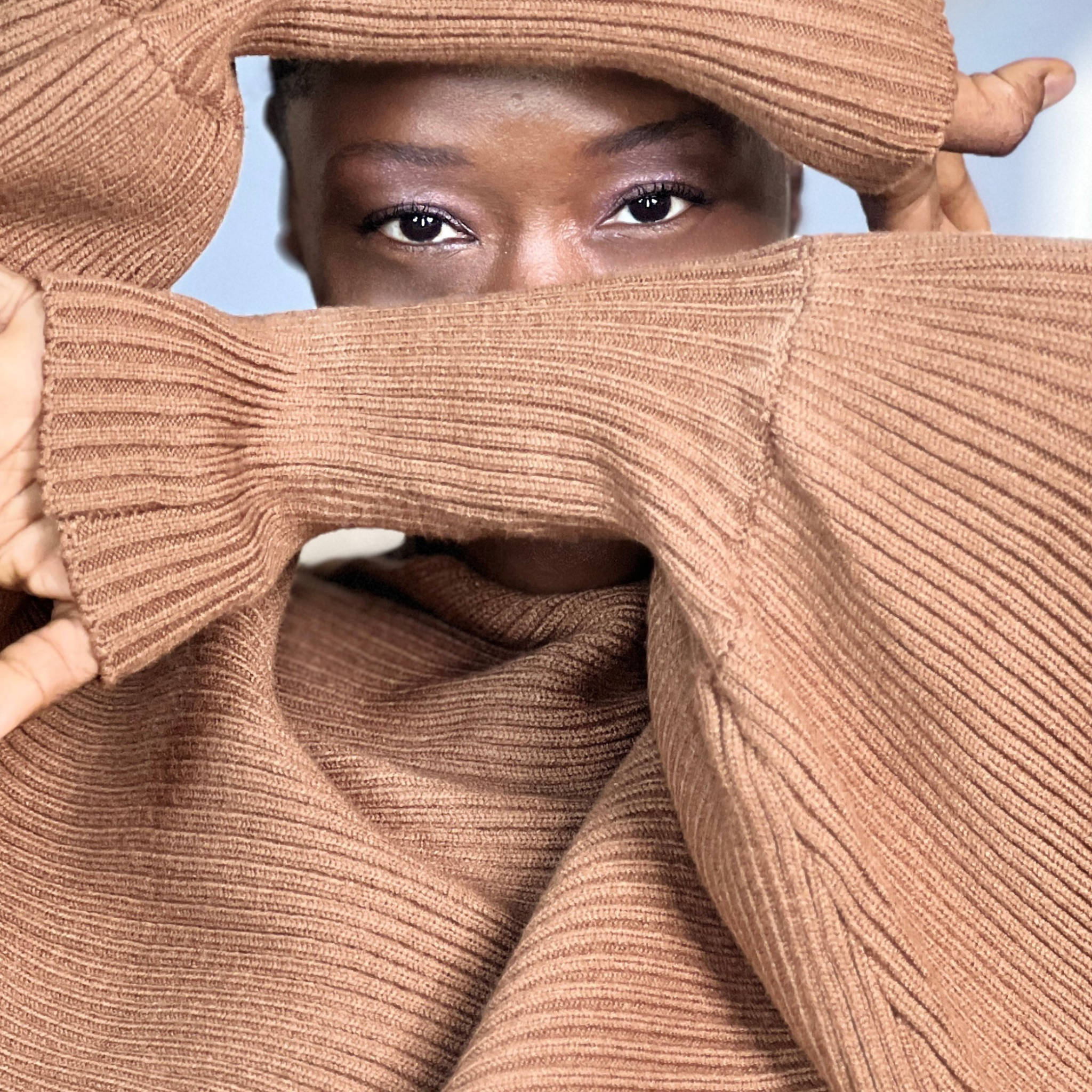 Person wearing a brown turtleneck sweater with a blurred background